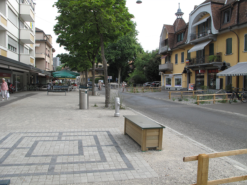 Fussgängerzone mit Bäumen, Strasse Restaurants und Versickerungsflächen mit Kies und Vegetationen versehen.